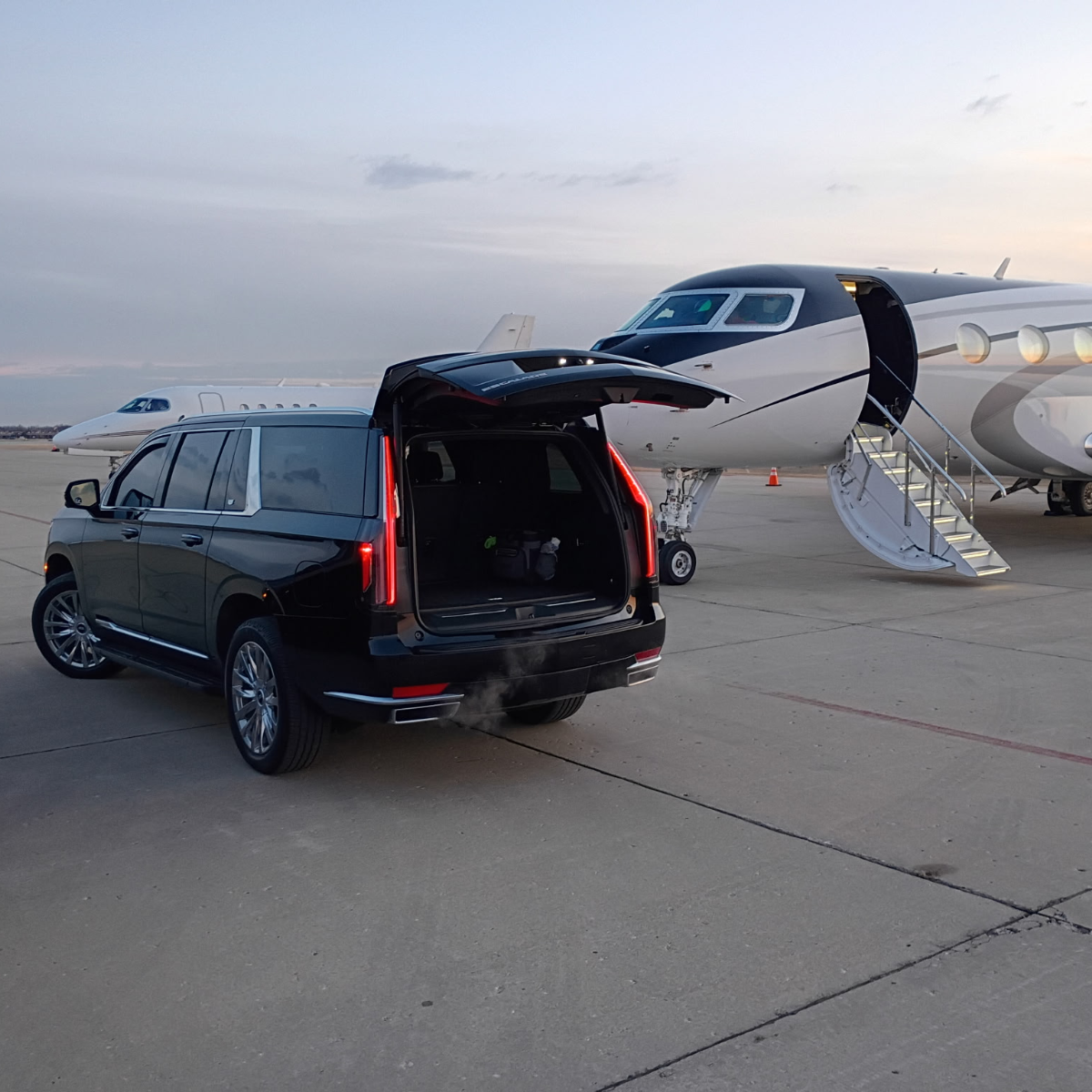 Black SUV with open trunk parked by a private jet on tarmac