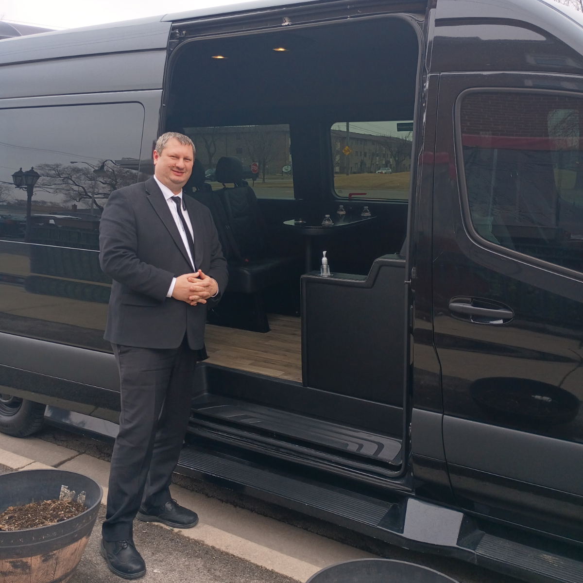 Senior executive chauffeur next to a black Sprinter van interior view